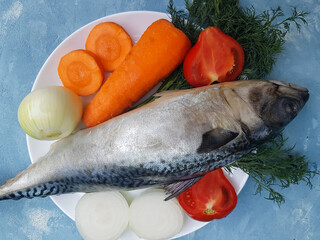Fresh mackerel fish on a plate with vegetables ingredients for cooking on a blue background