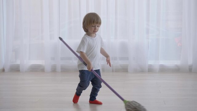 Funny child cleaning floor with mop, boy have fun, rotate, enjoy responsibility