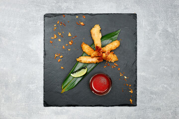 Restaurant set of fried king prawns with ketchup, lime, fried onions on a graphite board and gray background