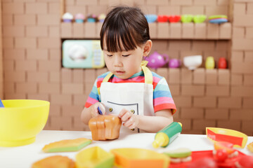 toddler girl pretend play food preparing role against cardboard blocks kitchen background
