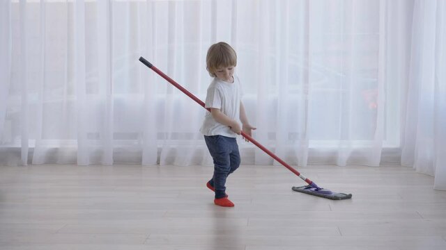 Smart funny child with mop cleaning careful floor using finger, meticulous work
