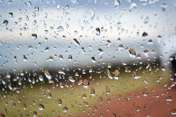 Glass window full of raindrops, blurred colors behind. Winter concept, looking outside from the comfort of a house.
