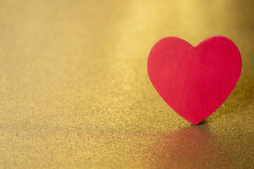 One single red heart  on a gold glitter and sequin background that sparkles and has lots of copy space for love and Valentine's Day
