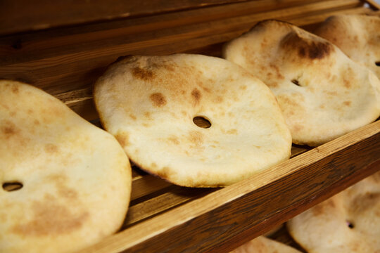 Round pita bread with a hole, flat unleavened white bread, tortilla baked in a tandoor. Ready fresh pita bread is on the wooden shelves in the store, close-up