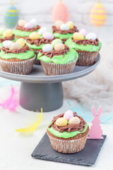Homemade carrot cake muffins decorated with cream cheese frosting and Easter chocolate eggs, on gray plate, vertical
