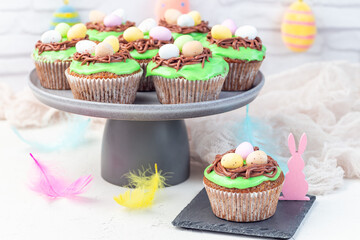 Homemade carrot cake muffins decorated with cream cheese frosting and Easter chocolate eggs, on gray plate, horizontal