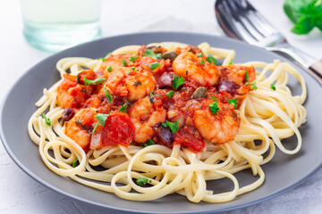 Linguine Puttanesca pasta with shrimps in spicy tomato basil sauce garnished with parsley, on gray plate, horizontal