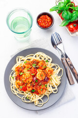 Linguine Puttanesca pasta with shrimps in spicy tomato basil sauce garnished with parsley, on gray plate, vertical, top view
