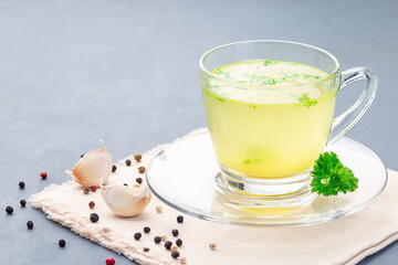 Homemade chicken broth in  glass cup garnished with chopped parsley, horizontal, copy space