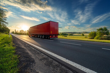 Red truck driving on the asphalt road in rural landscape at sunset