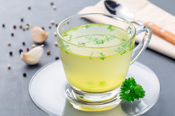 Homemade chicken broth in glass cup garnished with chopped parsley, horizontal