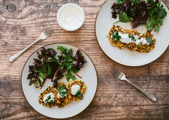 Zucchini fritters with green salad, yogurt on white plate on wooden table