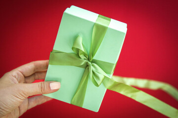 Girl holds a gift box and unties the bow. a girl opens a gift box. Gift box on a red background. Girl unties the tape from the box.
