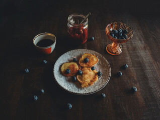 Fototapeta na wymiar side view of a white vintage plate with pancakes and fresh blueberries and a cup of coffee with a jar of jam on a dark wooden table