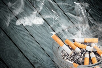 Ashtray and smoked cigarettes with smoke on desk
