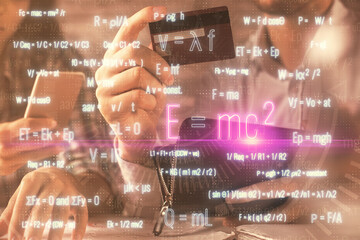 Double exposure of man and woman on-line shopping holding a credit card and formulas hologram...