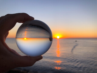 Woman's hand holding a crystal ball, looking through to sea and sky at dawn. Creative Concept,...