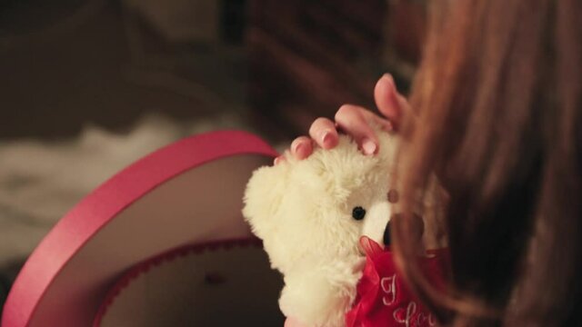 A girl takes a teddy bear out of a red box and caresses it