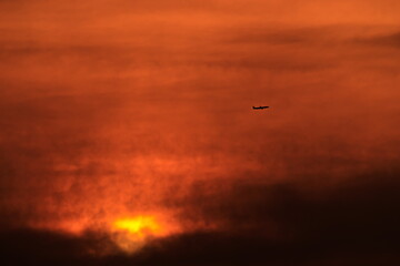 plane flying at high altitude, crossing a reddish sky during twilight.