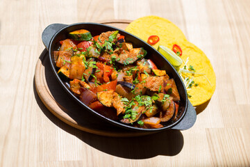 Spicy fajitos in cast iron pan and mexican tortillas on wooden table on sunny day, top view