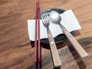 Set of cutlery, chopsticks on paper, placed on a wooden table.