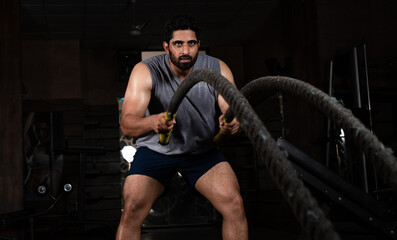 Fototapeta na wymiar Asian Indian man Doing exercise with Battle rope in Gym