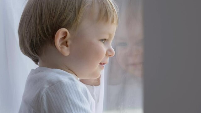 Happy child portrait smiling and looking out the window, baby boy wishing to go outside, white curtains