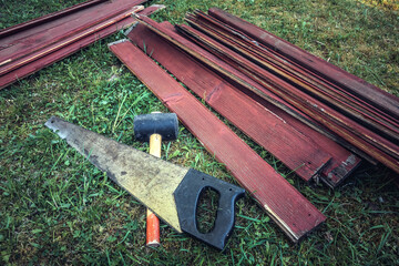 Hacksaw, rubber mallet and wooden planks on the grass in the garden