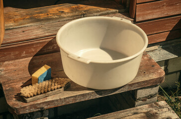 Fototapeta na wymiar Plastic white basin and brush for washing on wooden steps in the garden