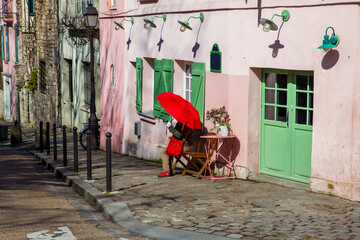 Lady with a red umbrella sitting in front of a pink house in the famous Montmartre neighborhood