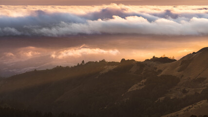 Sunset landscape in Santa Cruz mountains with sunlight illuminating a valley covered by a blanket...
