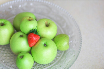 On a transparent plate green apples and red strawberries. Contrast. High quality photo