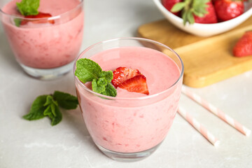 Tasty strawberry smoothie with mint in glass on light grey table