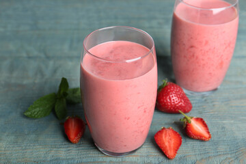 Tasty strawberry smoothies in glasses on blue wooden table