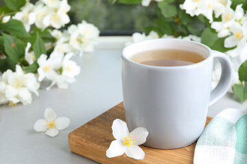 Fototapeta na wymiar Cup of tea and fresh jasmine flowers on light grey table. Space for text