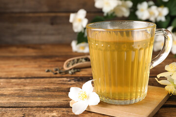 Cup of tea and fresh jasmine flowers on wooden table. Space for text