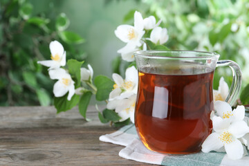Cup of tea and fresh jasmine flowers on wooden table. Space for text