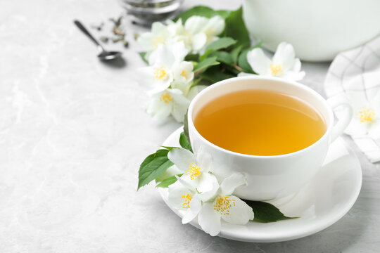 Cup of tea and fresh jasmine flowers on light grey marble table. Space for text