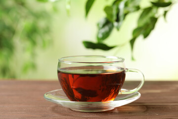 Cup of black tea on wooden table against blurred background. Space for text