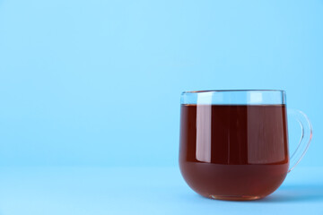 Glass cup of aromatic black tea on light blue background, space for text
