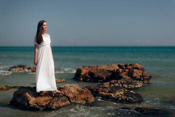 Fototapeta na wymiar Woman with Long Dress Standing on Rocks By the Sea