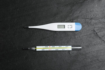 Mercury and digital thermometers on black slate background, flat lay
