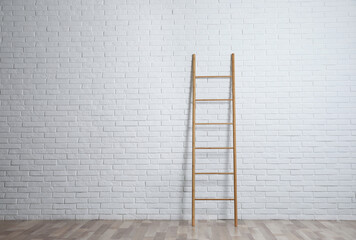 Modern wooden ladder near white brick wall