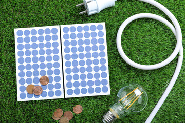 Flat lay composition with solar panels, light bulb and coins on green grass