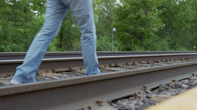 High quality 4k video of a young man who is walking on the railway away from the camera, focus on legs. Men wearing jeans and sport jacket.