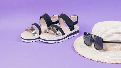 A woman's hat with sunglasses and sandals on a purple background.