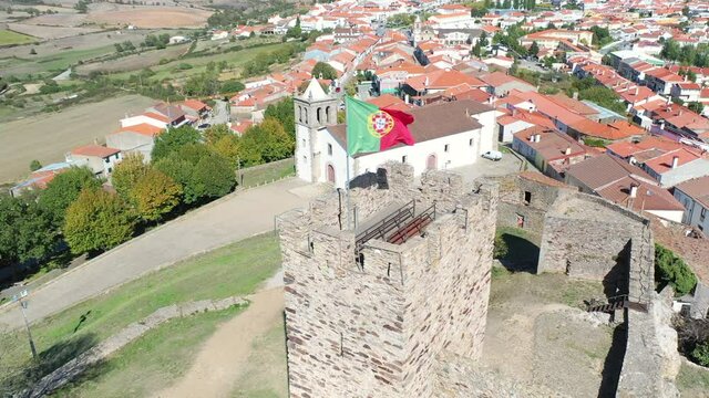 (flying around a POI) Portuguese flag on the castle tower and a cityscape of Mogadouro town, district of Braganca, Tras-os-Montes, Portugal
