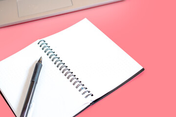 home-a woman's place, a laptop and an open notebook with white blank sheets of paper for text on a pink background