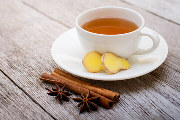 Closeup white ceramic cup of hot ginger tea with fresh organic ginger slice and cinnamon isolated on old wood table background .
