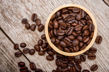 Closeup dark brown coffee beans in wooden bowl isolated on old wood table background. Top view. Flat lay.